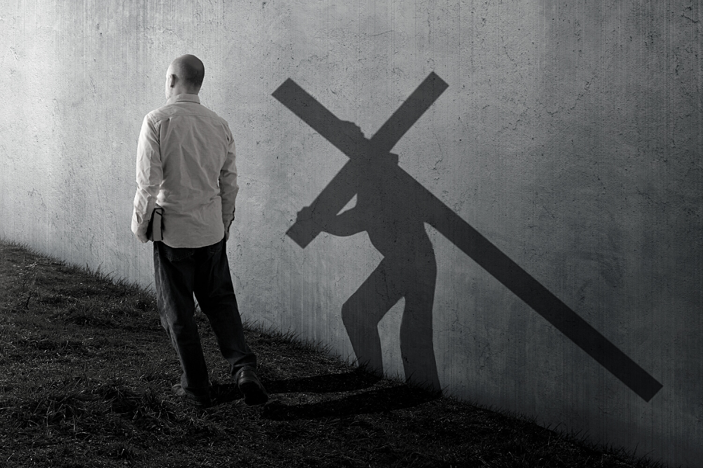 Man holding a Bible with his shadow showing him carrying a cross on his back.